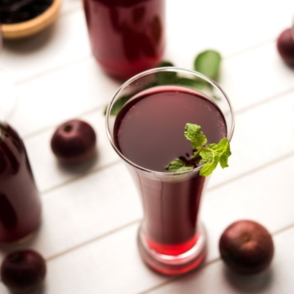 A glass of tart cherry juice garnished with mint, surrounded by fresh cherries on a white table, highlighting the benefits of tart cherry juice for sleep.